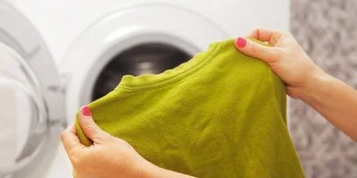 Ruce drží zelené tričko před otevřenou pračkou.
