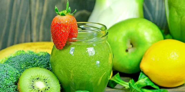 Zelený smoothie s ovocem a zeleninou na dřevěném pozadí.