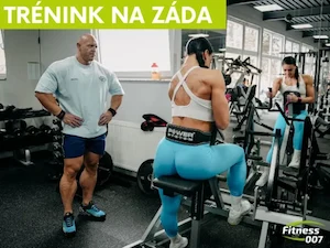 Žena cvičí na strojích pro posilování stehenních svalů pod dohledem trenéra.