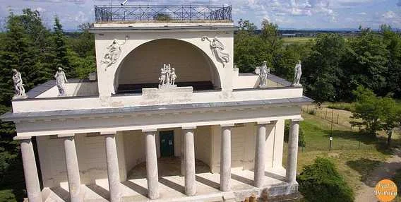 Bílá novoklasická pavilón s sloupy v zeleném parku u Hlohovce.